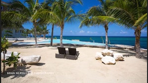 A beach with palm trees, lounge chairs, and a pool. - Whispering Seas (Tower Isle)