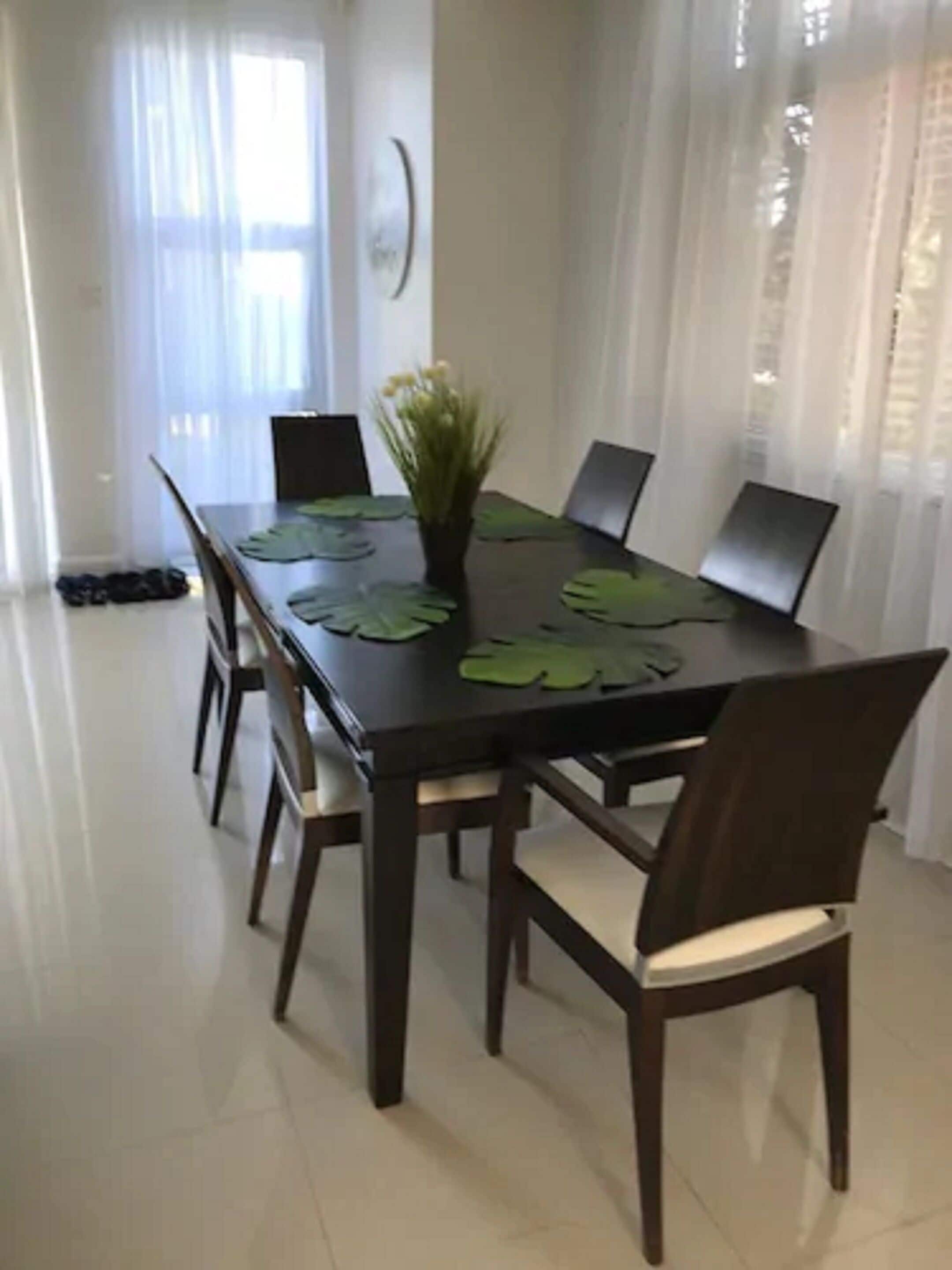 Un espace repas avec une longue table, six chaises et une plante en pot placée au centre.