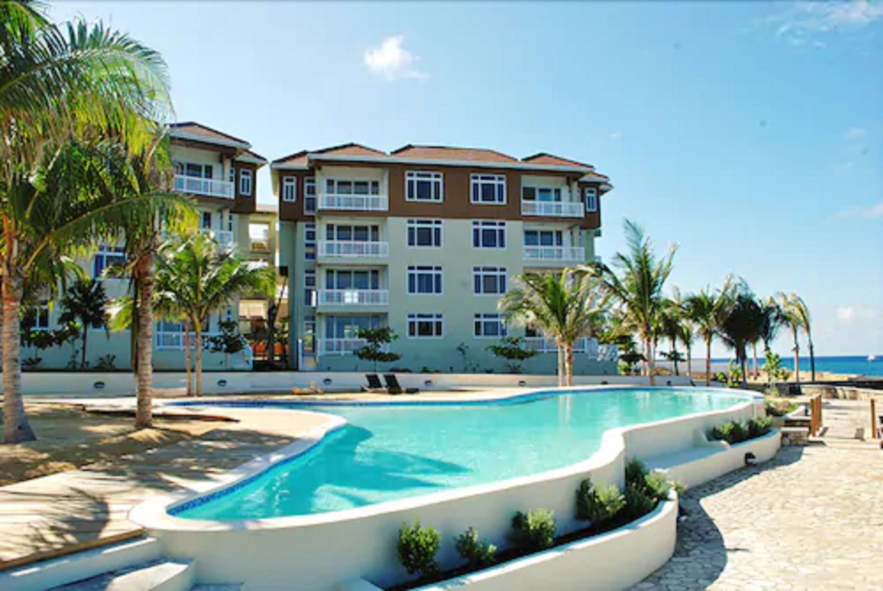 Um resort com piscina, palmeiras e vista para a praia.