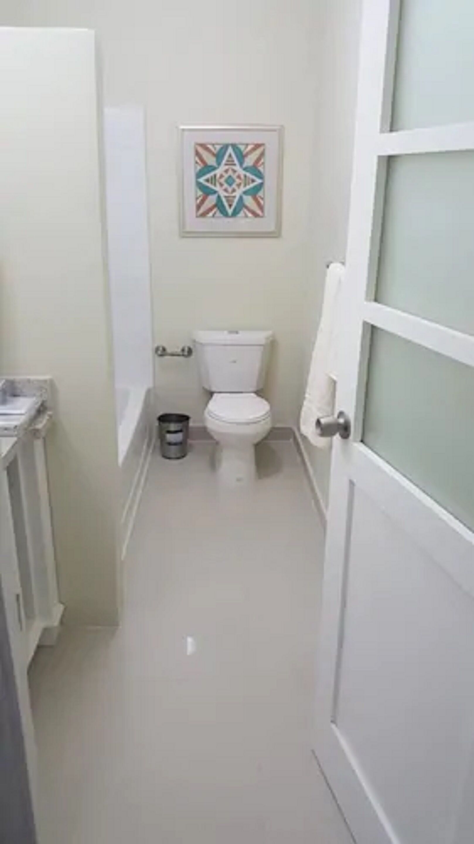 A narrow hallway leading to a toilet with a geometric-patterned artwork above it.