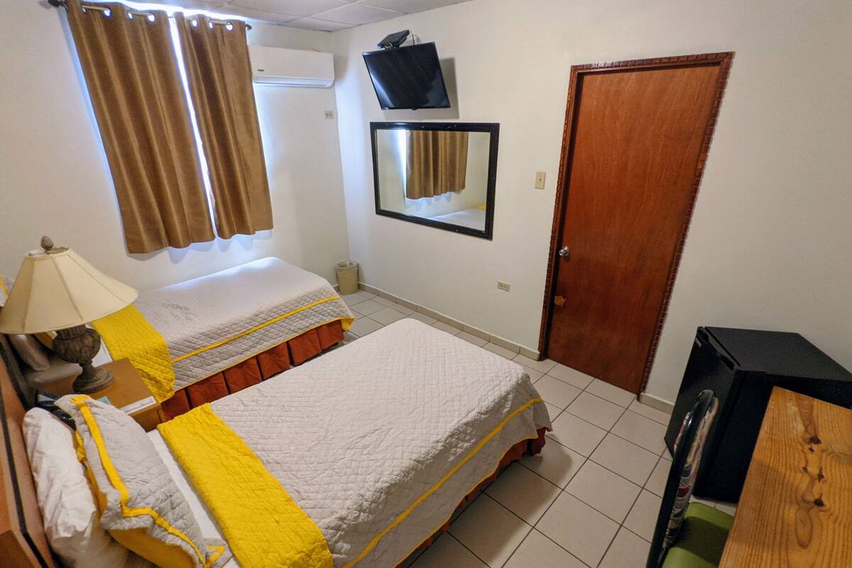 A hotel room with two beds, a TV mounted on the wall, a wooden door, and a trash bin.
