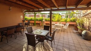 An outdoor patio with wooden beams, tiled flooring, and a variety of seating arrangements including tables and chairs.