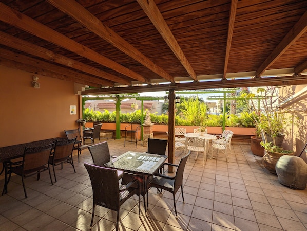 An outdoor patio with wooden beams, tiled flooring, and a variety of seating arrangements including tables and chairs. - Hotel San Jorge (San Juan)
