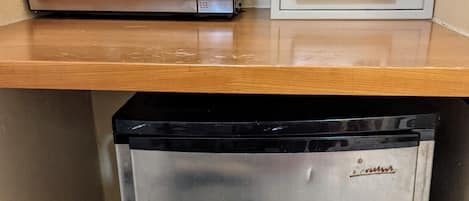 A compact kitchen area with a microwave, a small refrigerator, and a safe on the countertop.