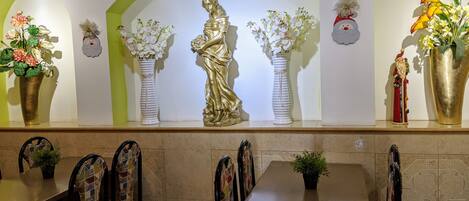 Un restaurante con una barra que exhibe arreglos florales, una estatua y una figura de Papá Noel. Mesas y sillas están dispuestas al frente.