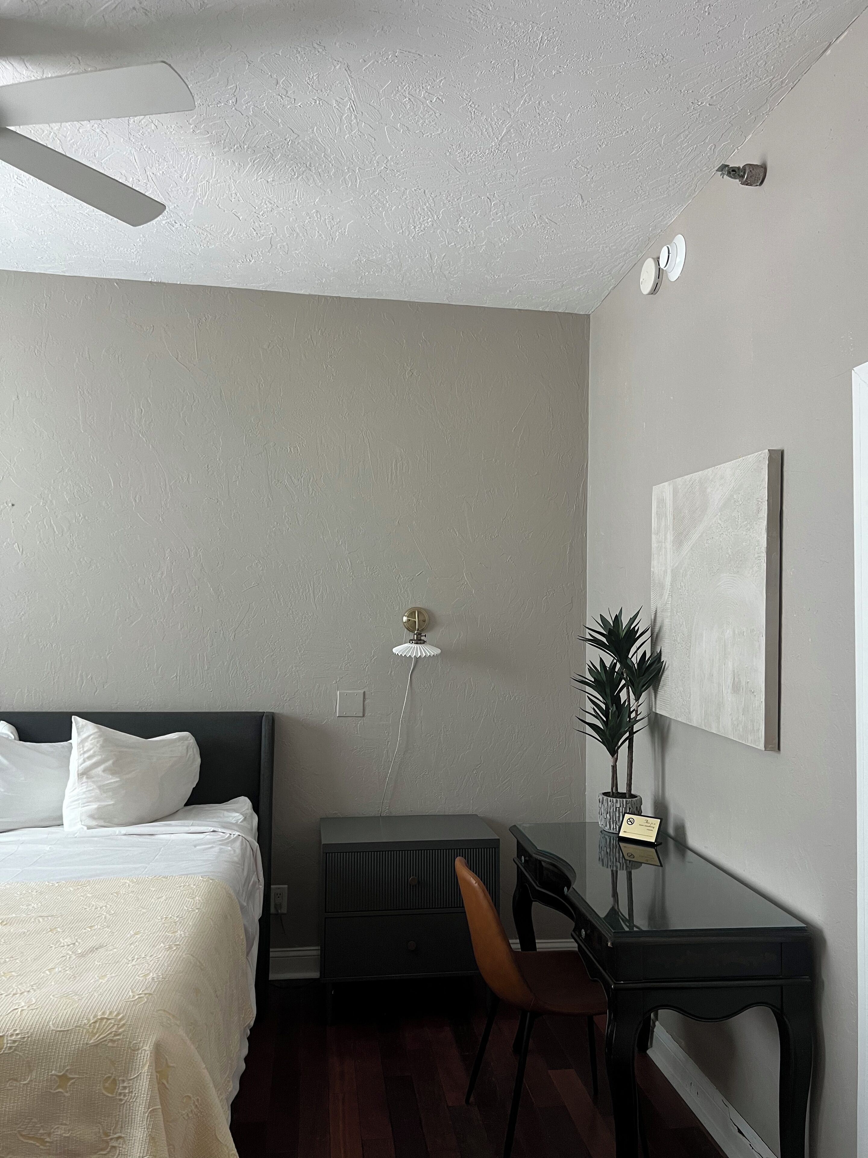 A bedroom with a bed, a desk, a chair, a radiator, and a ceiling fan.