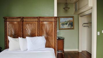 Una cama bien hecha con cabecera de madera, un cuadro en la pared y un pasillo que conduce a otra habitación.