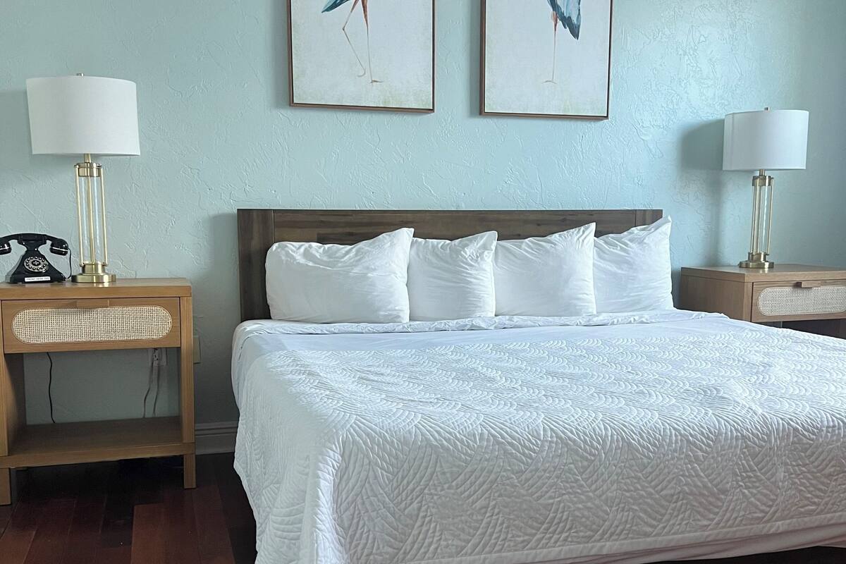 A neatly made bed with white linens, two bedside tables with lamps, and two framed wall art pieces of birds.