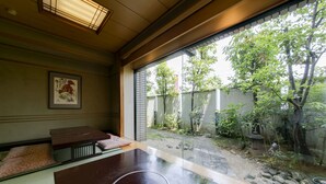 Een traditionele Japanse kamer met tatami vloerbedekking, een lage houten tafel en uitzicht op een tuin door een glijdende deur.