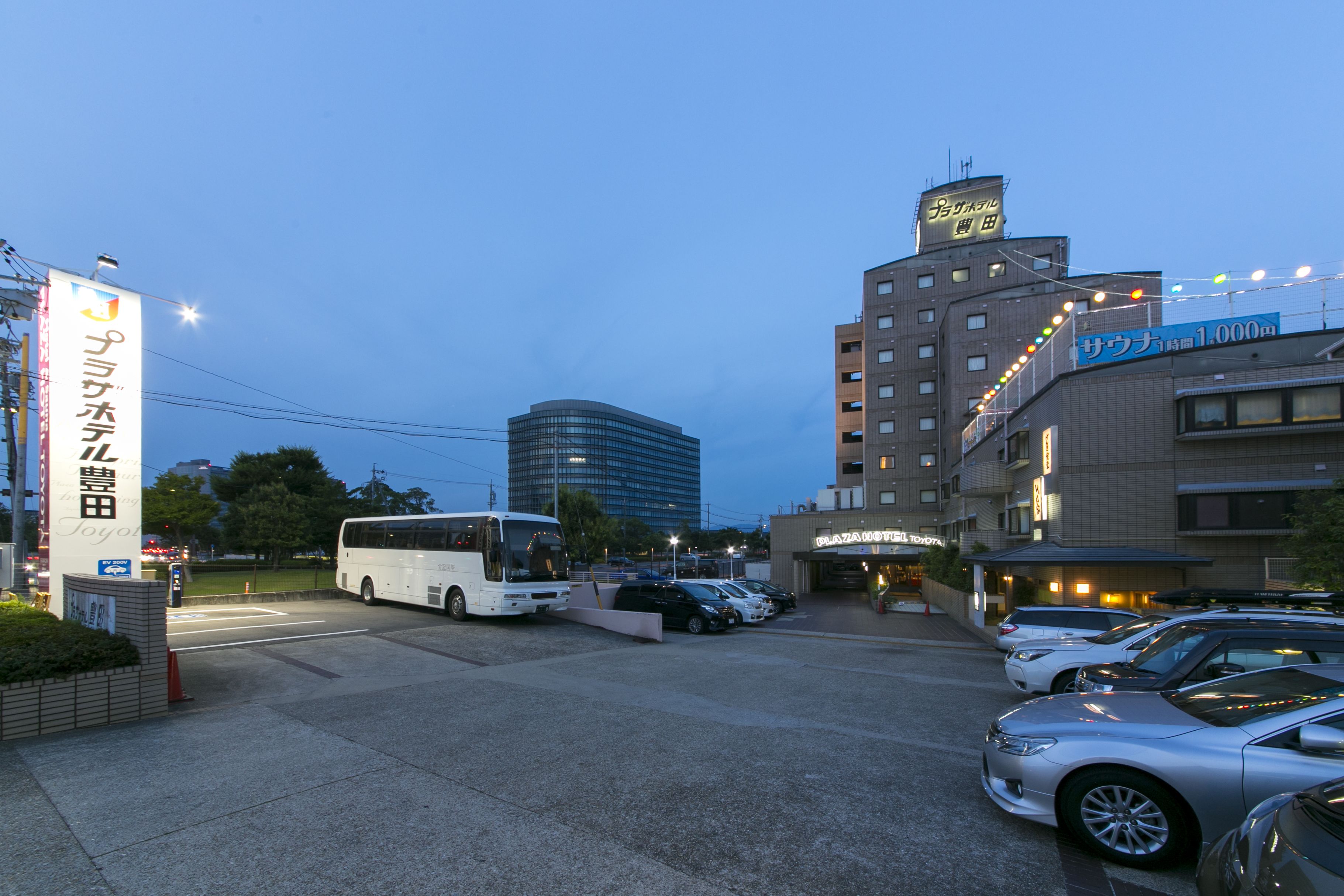 A parking lot with several cars and a bus, a building with a sign that reads "SAWADA," and another sign that says "TOYOTA."