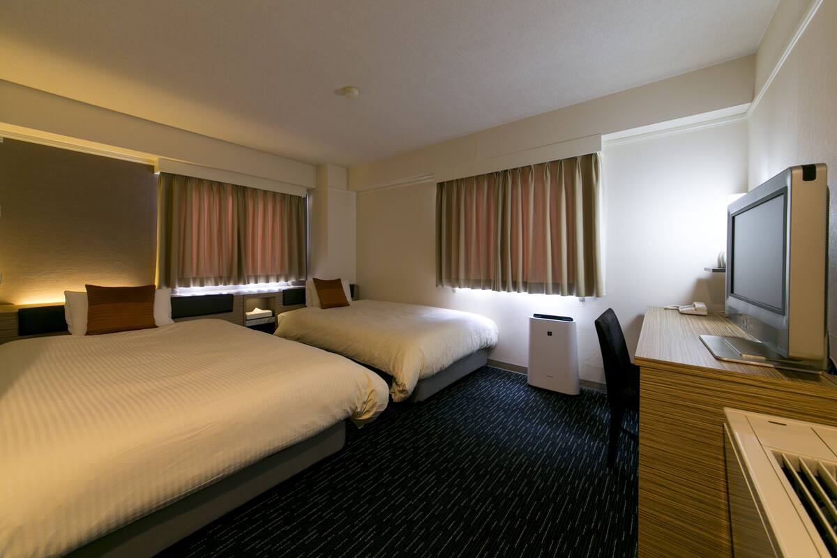 Une chambre d’hôtel avec deux lits, un bureau avec un ordinateur, une télévision et une fenêtre avec des rideaux.