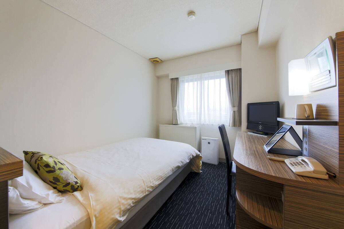 Une chambre d’hôtel équipée d’un lit, d’un bureau avec un ordinateur, d’un téléphone et d’une télévision.