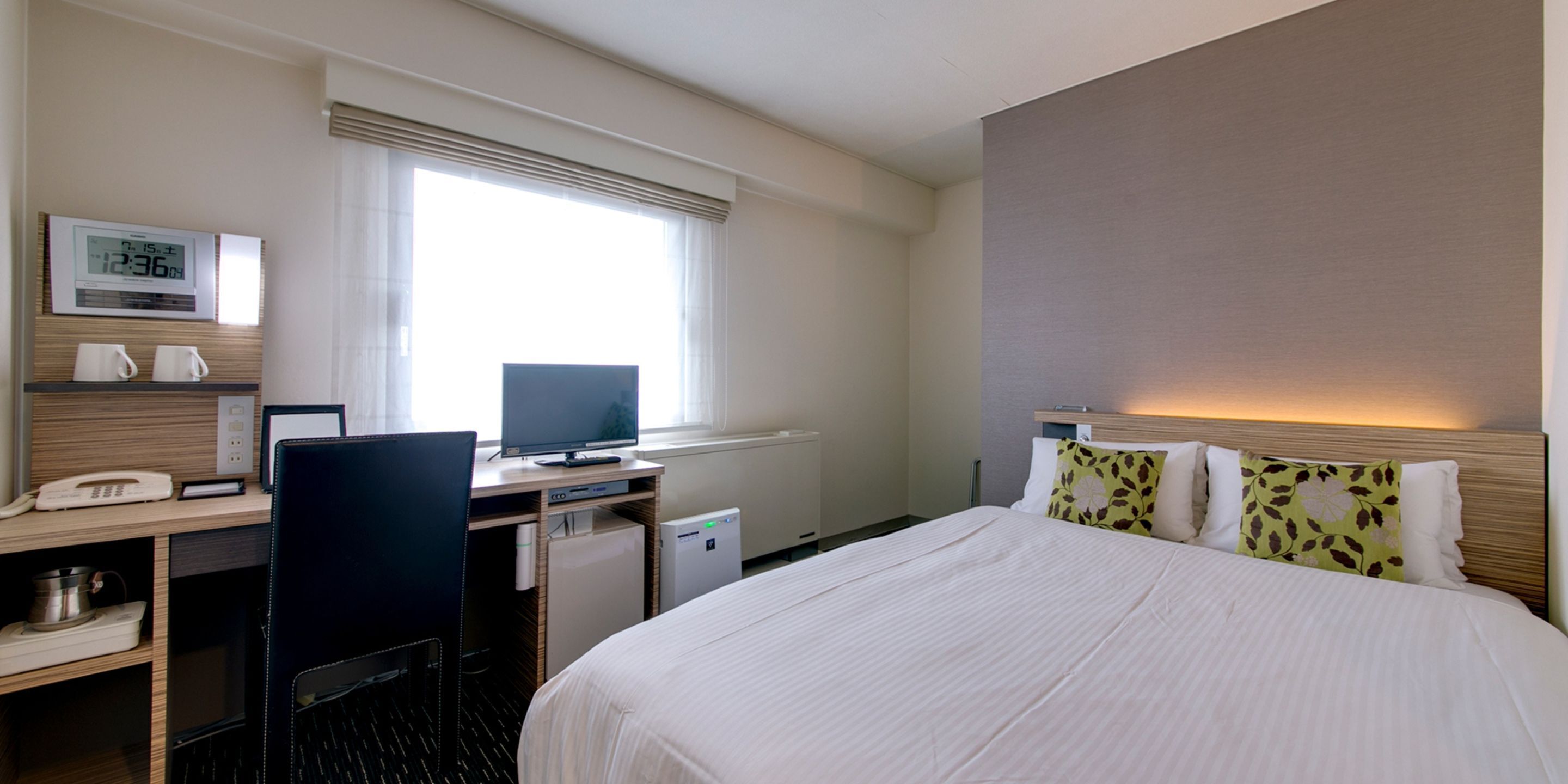 A hotel room with a bed, desk, chair, and a small kitchenette.