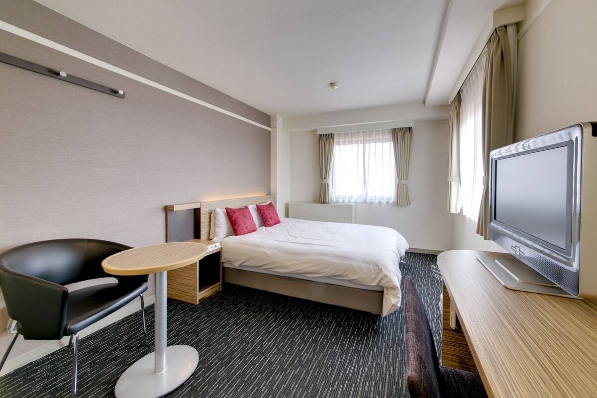 Une chambre d’hôtel équipée d’un lit, d’un bureau, d’une chaise, d’une télévision et d’une fenêtre avec des rideaux.