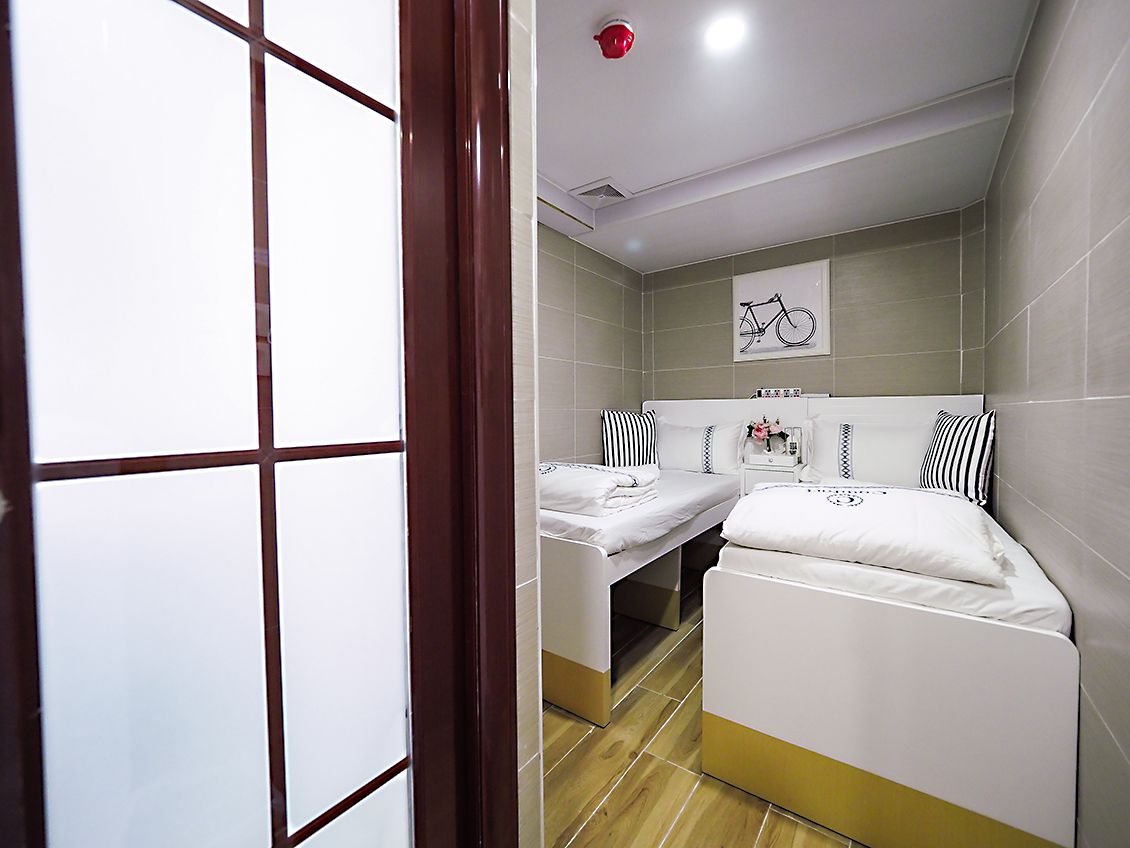 A hotel room with two beds, a bicycle-themed artwork on the wall, and a red ceiling light.
