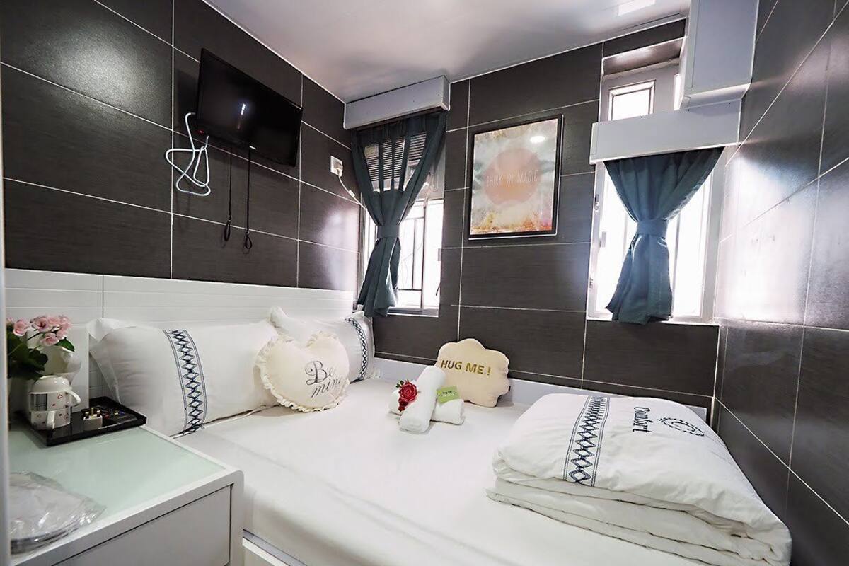 A modern hotel room with a large bed, a flat-screen TV mounted on the wall, and a window with curtains.