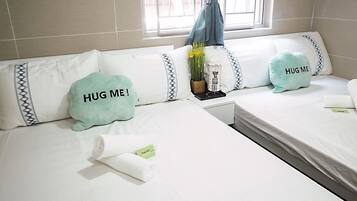 A hotel room with two beds, each with a pillow that says "HUG ME!" and a small table with a vase of flowers.
