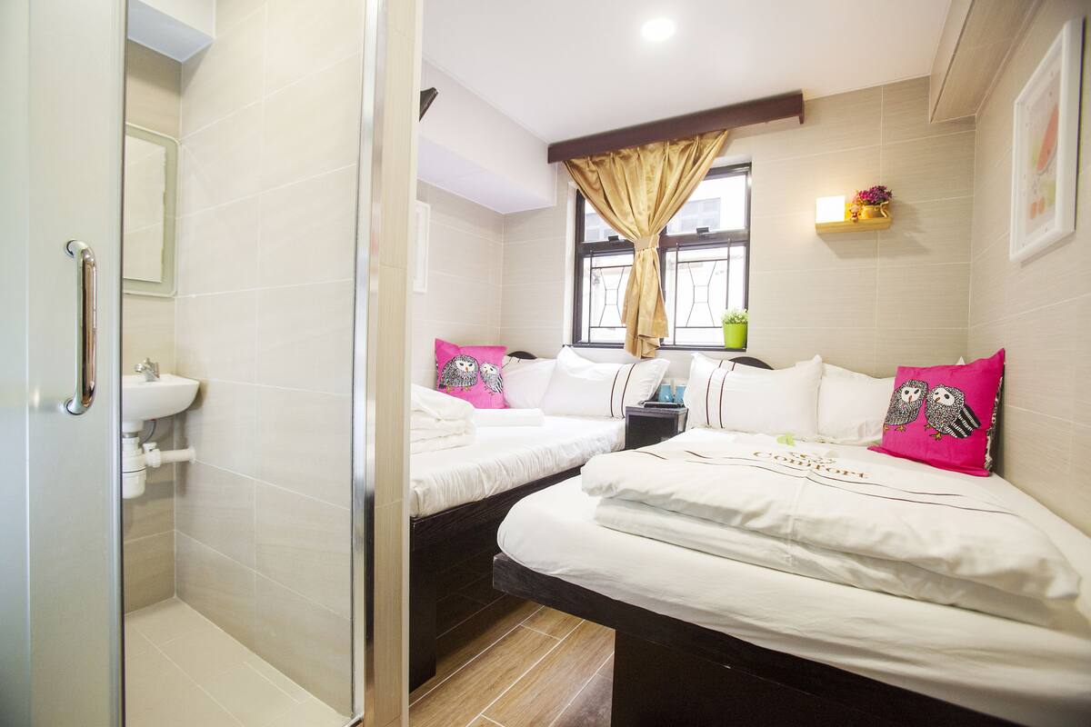 A hotel room with two beds, a shower, a sink, and a window with curtains.
