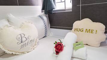 A neatly arranged hotel room with a bed, pillows, a rolled towel, and a decorative rose.