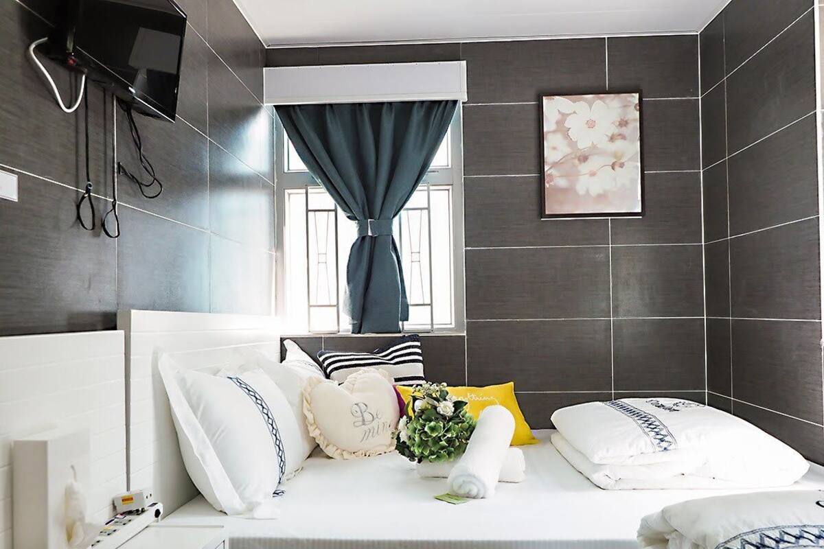A modern hotel room with a bed, a window with curtains, a mounted TV, and a painting on the wall.