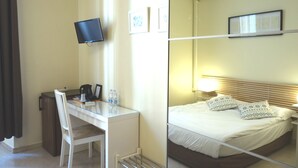 Ein Hotelzimmer mit Schreibtisch, Stuhl, Bett und einem an der Wand befestigten Fernseher.