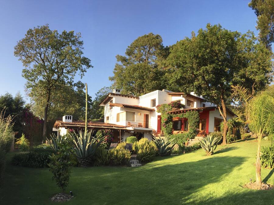 A two-story house with a patio, surrounded by lush greenery and trees.