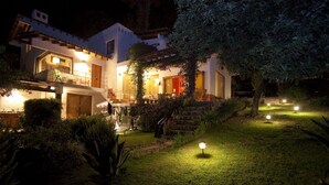 Une maison moderne dotée d’un jardin bien éclairé la nuit, avec une terrasse et un espace salon extérieur.