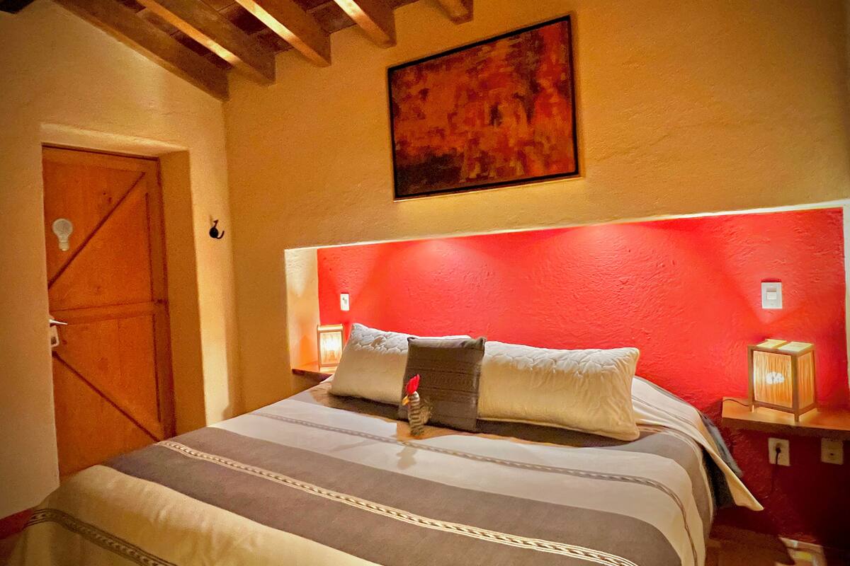 Ein Schlafzimmer mit einem Bett, Holzbalkendecke, einer roten Akzentwand und einem Gemälde über dem Bett.