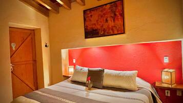 Un dormitorio con cama, vigas de madera en el techo, una pared de acento roja y un cuadro sobre la cama.