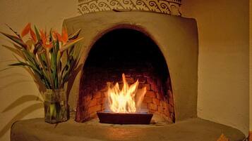 Una chimenea de piedra con fuego encendido, un diseño decorativo en la pared superior y un jarrón de flores a la izquierda.