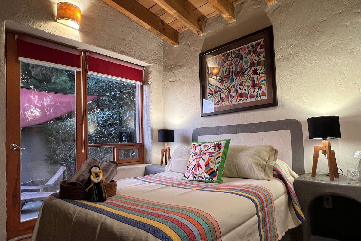 Ein Schlafzimmer mit Bett, einem Fenster mit Blick, einem gerahmten Kunstwerk und einer Lampe auf einem Nachttisch.