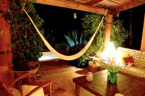 A hammock, wicker furniture, a table with a vase, and a couch in an outdoor setting at night. - Las Luciérnagas (Valle de Bravo)