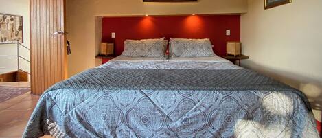 A bedroom with a red headboard, patterned bedding, and a painting above the bed.