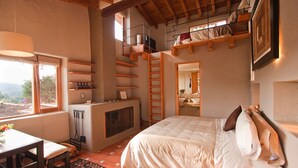 Une chambre avec un lit, une cheminée, une fenêtre donnant sur un beau paysage, des étagères en bois et un espace en mezzanine.