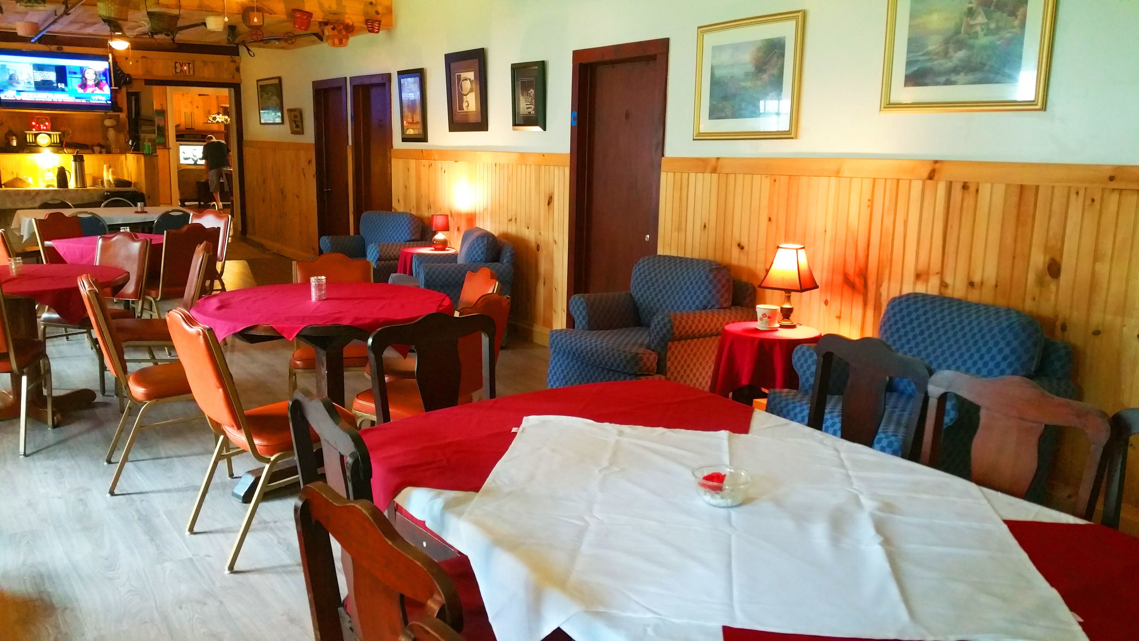 Un ristorante con rivestimenti in legno, tovaglie bianche e rosse e diversi posti a sedere, tra cui sedie e divani.