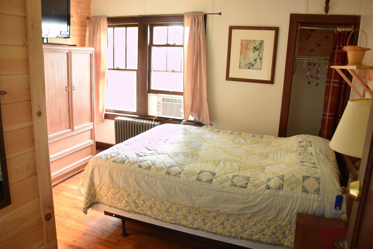 A bedroom with a bed, wooden wardrobe, radiator, window with curtains, and a framed picture on the wall.