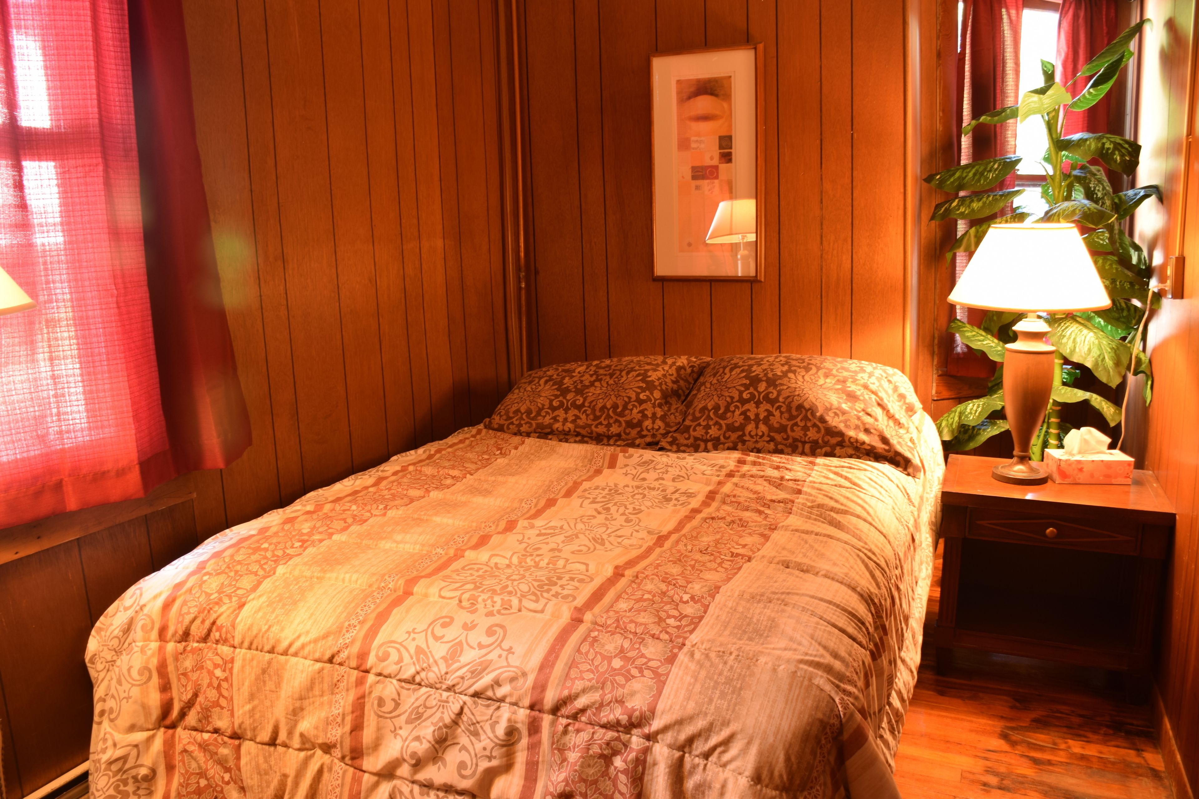 Un dormitorio con cama, mesita de noche, lámpara y planta en maceta.