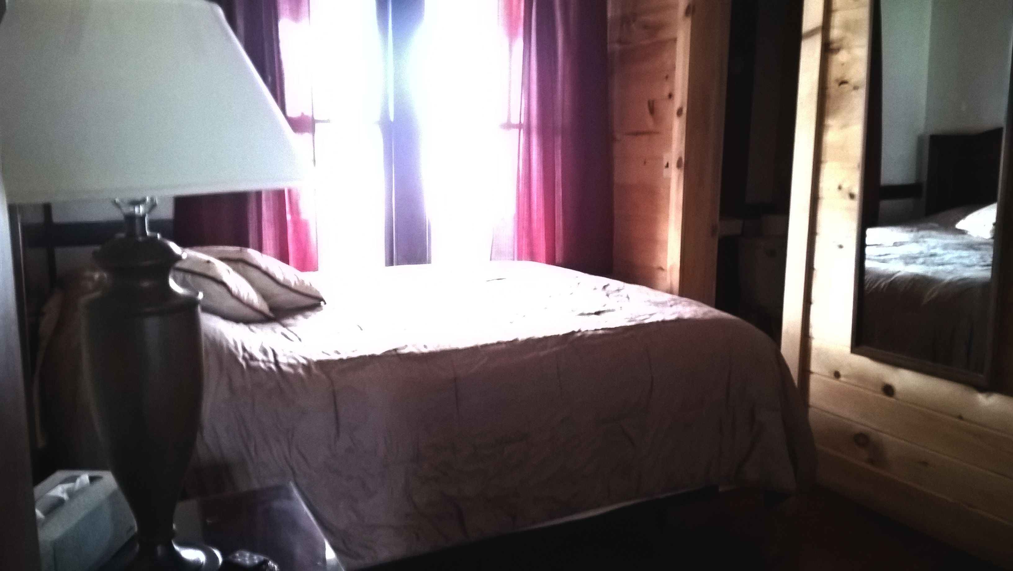 A bedroom with a bed, a lamp, and a window with curtains.