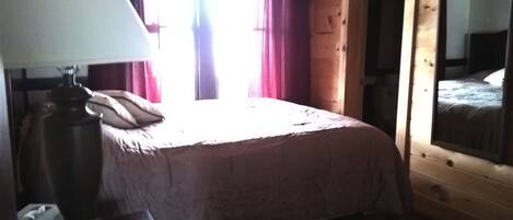 A bedroom with a bed, a lamp, and a window with curtains.