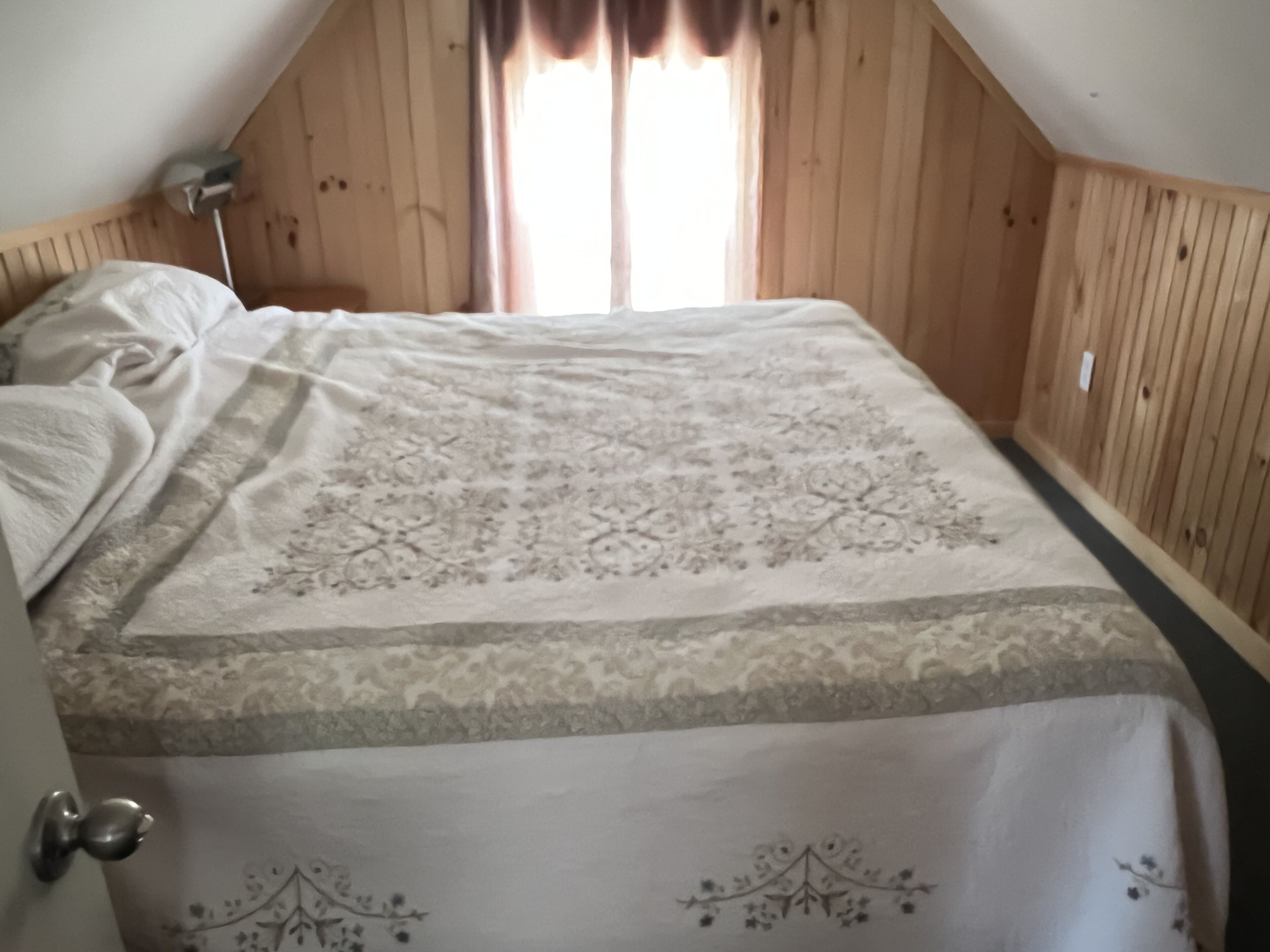 Un dormitorio con techo de madera, cama con colcha estampada y ventana con cortinas.
