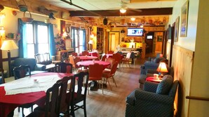 A restaurant with multiple tables and chairs, a bar area, and a television screen. - The Baseball Hotel (Richfield Springs)