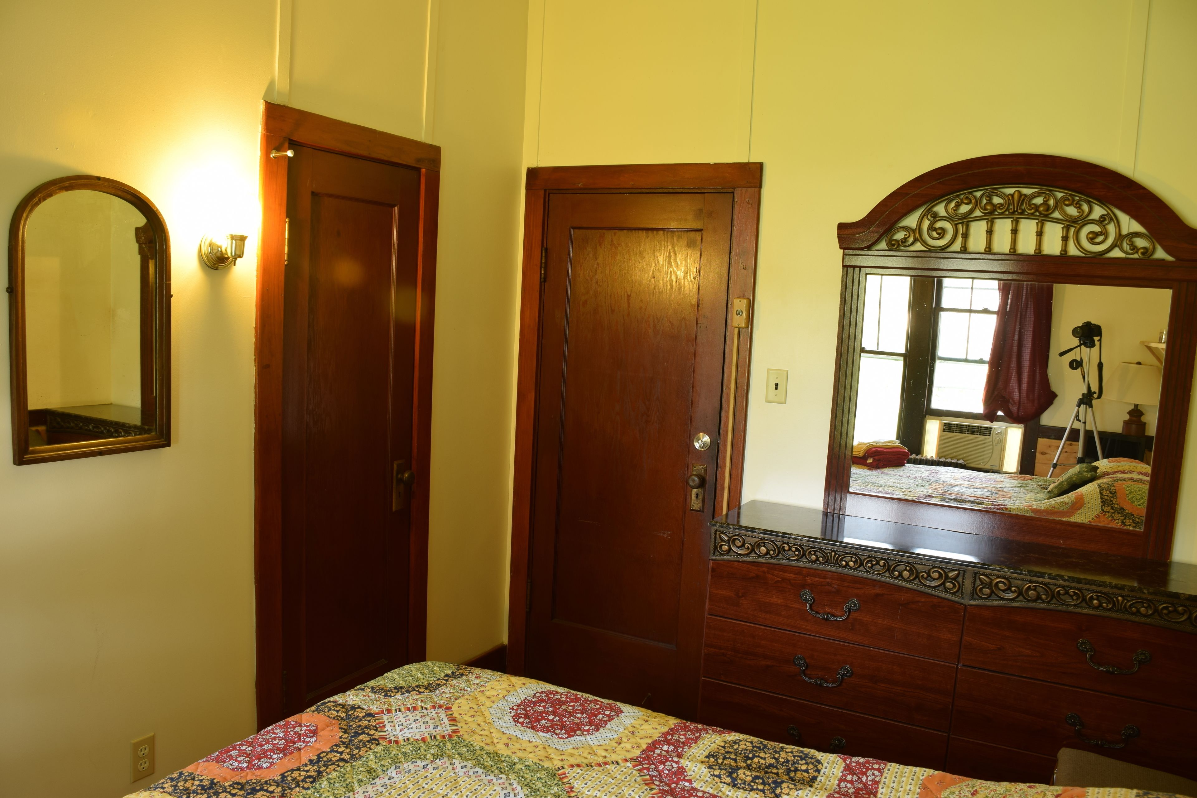 A bedroom with a wooden dresser, a mirror, and a quilted bedspread.