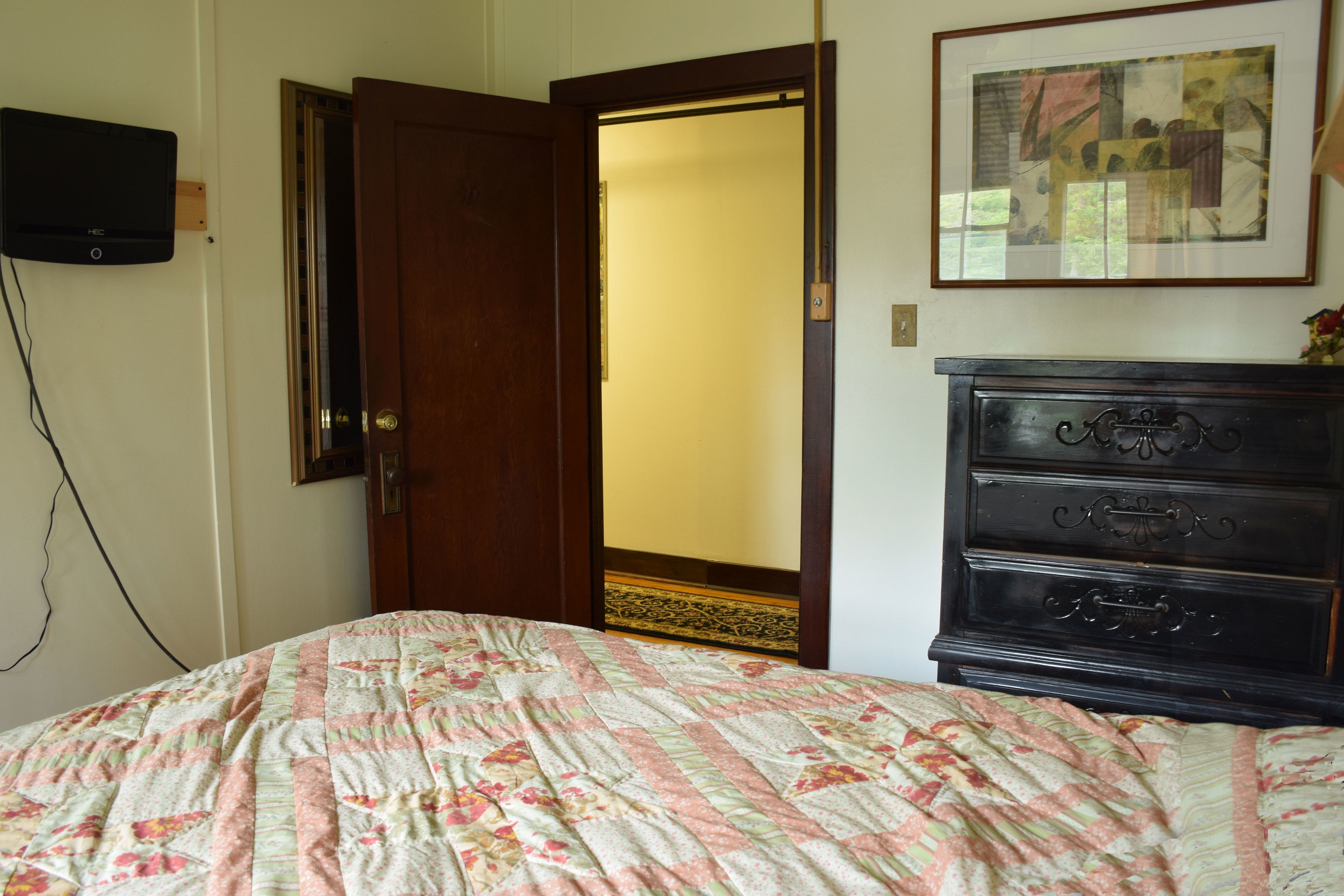 Un dormitorio con una cama, un aparador, una puerta, un televisor y un cuadro en la pared.