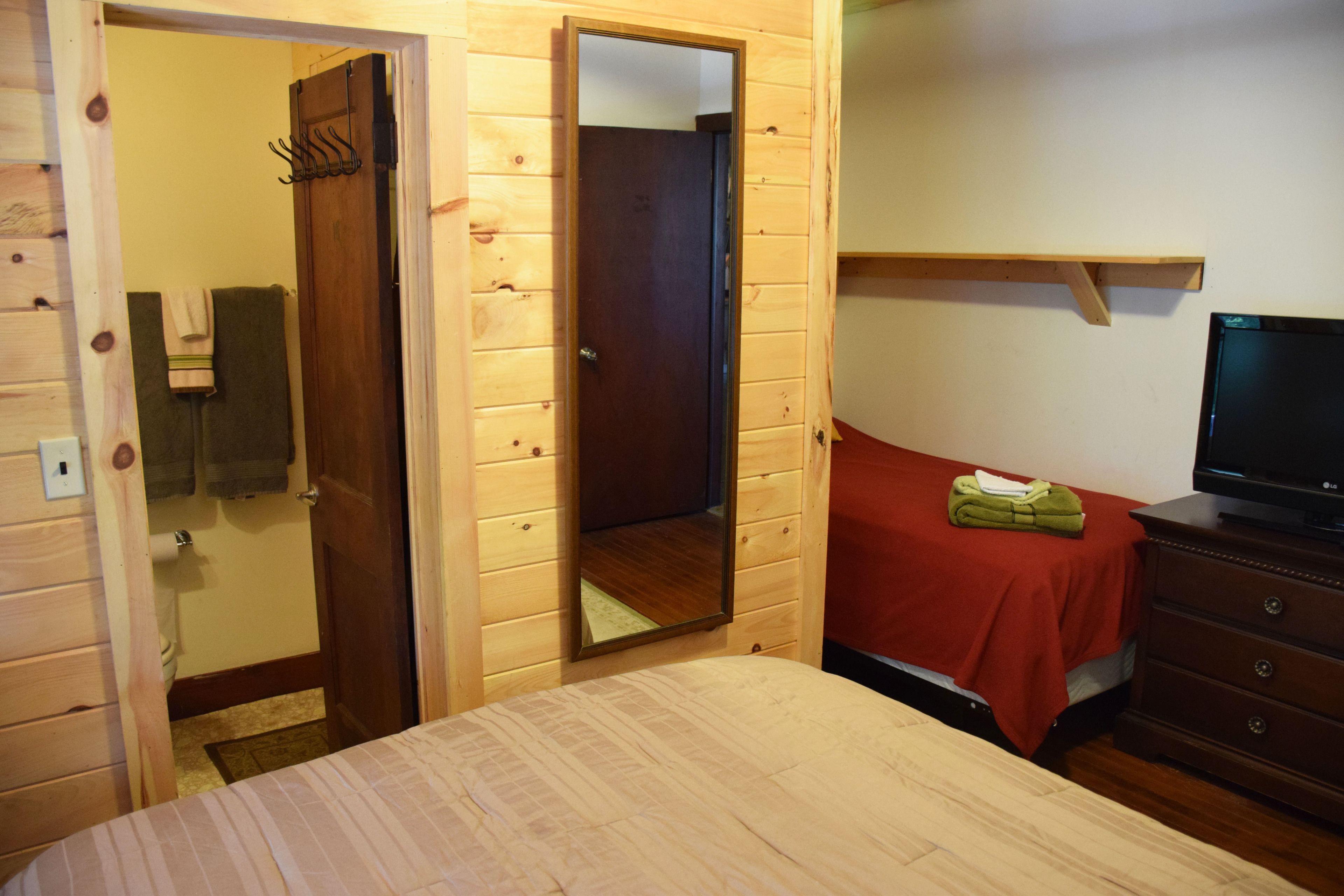 Habitación con paneles de madera, una cama, un aparador, un televisor y un espejo.