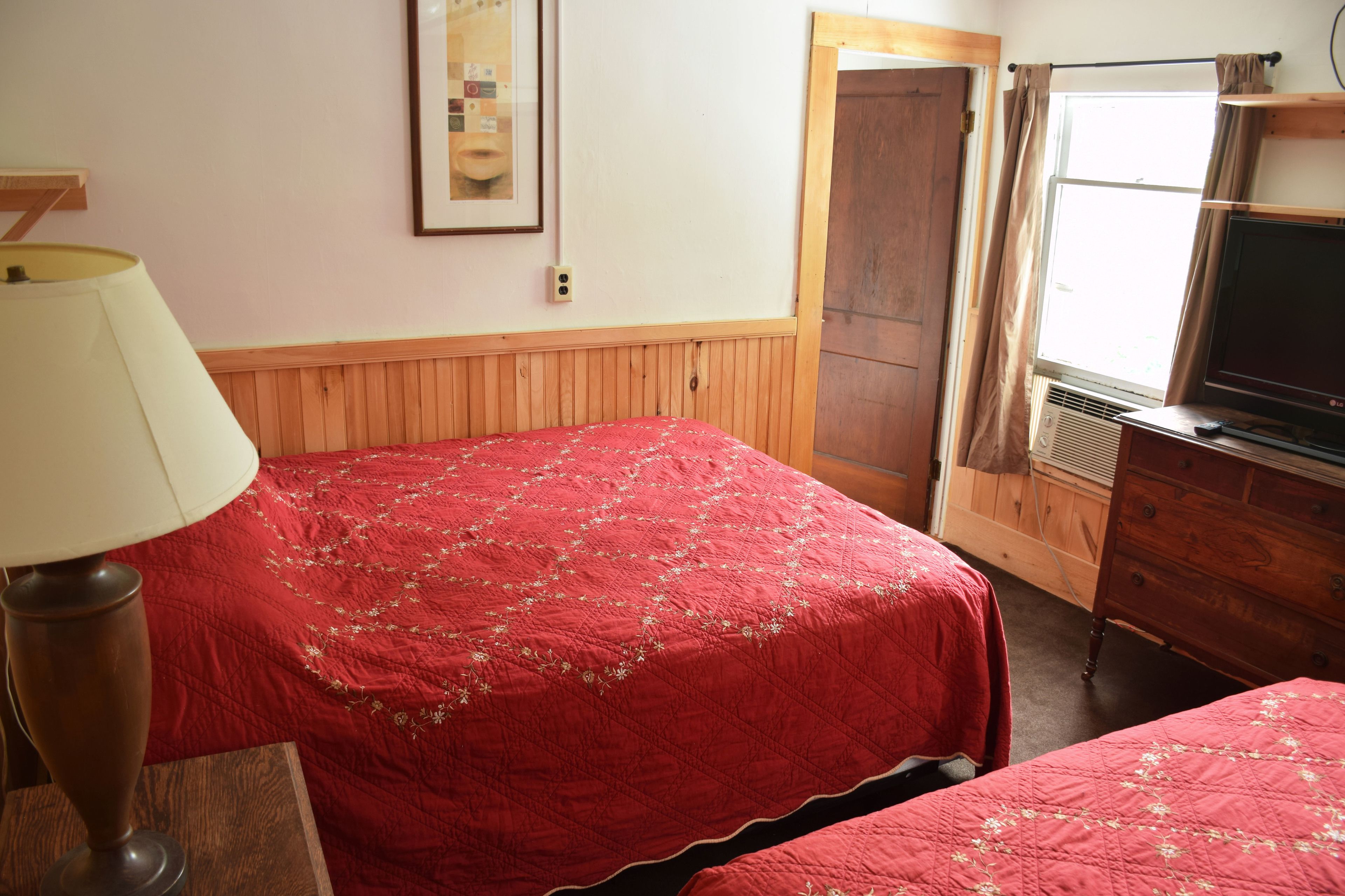Une chambre avec deux lits, une commode en bois, une télévision et une lampe.