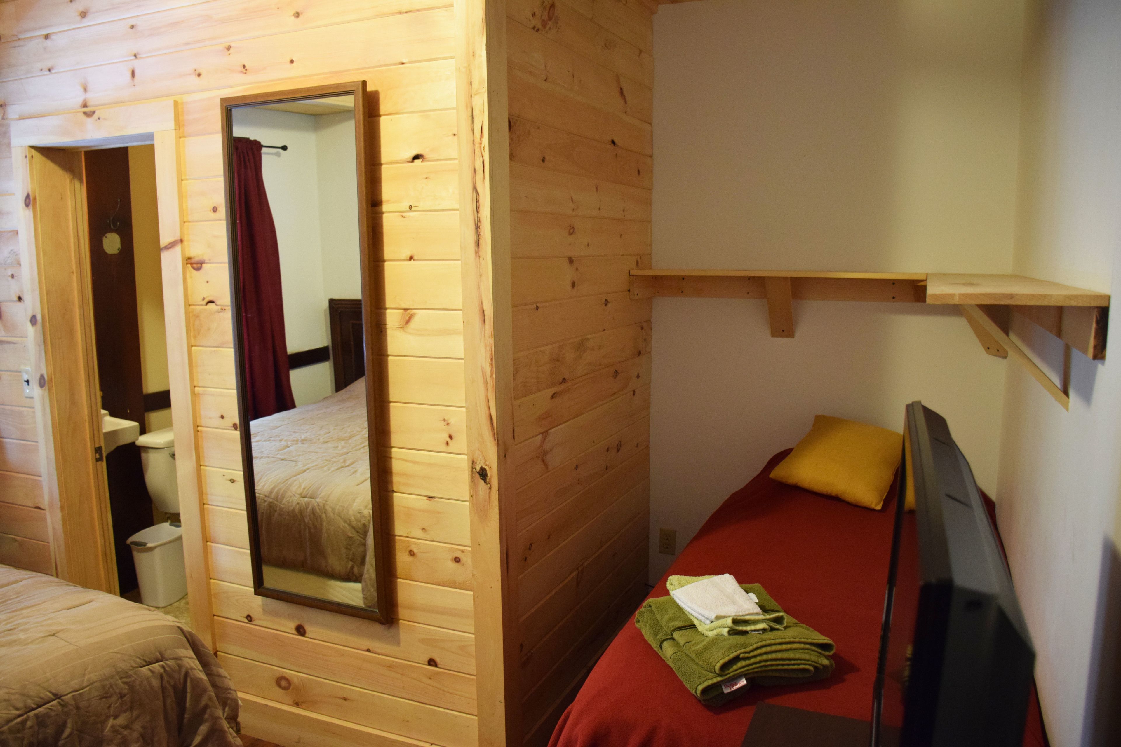Habitación de cabaña de madera con cama, espejo, televisor y una pequeña estantería.