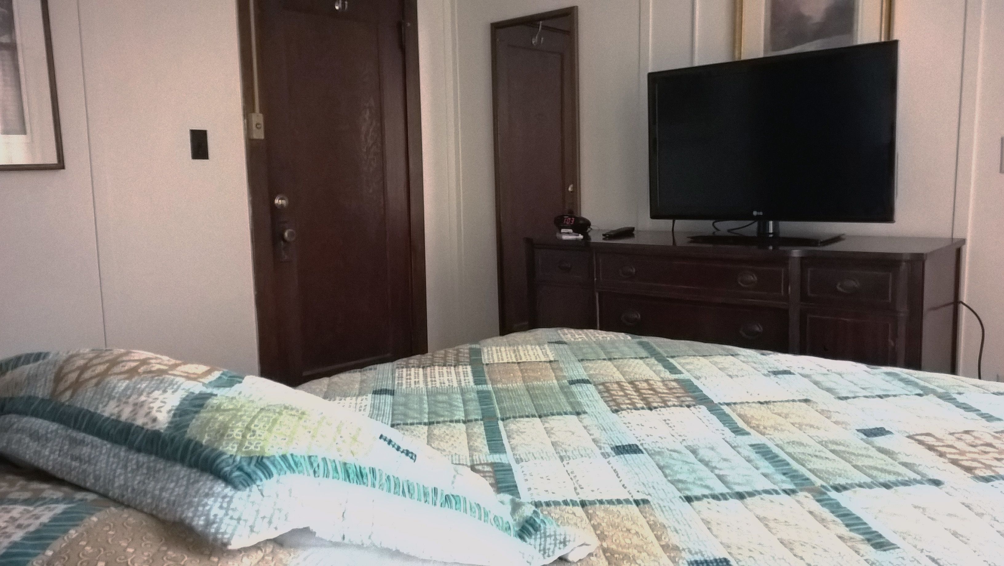Un dormitorio con cama, cómoda, televisor y una puerta.