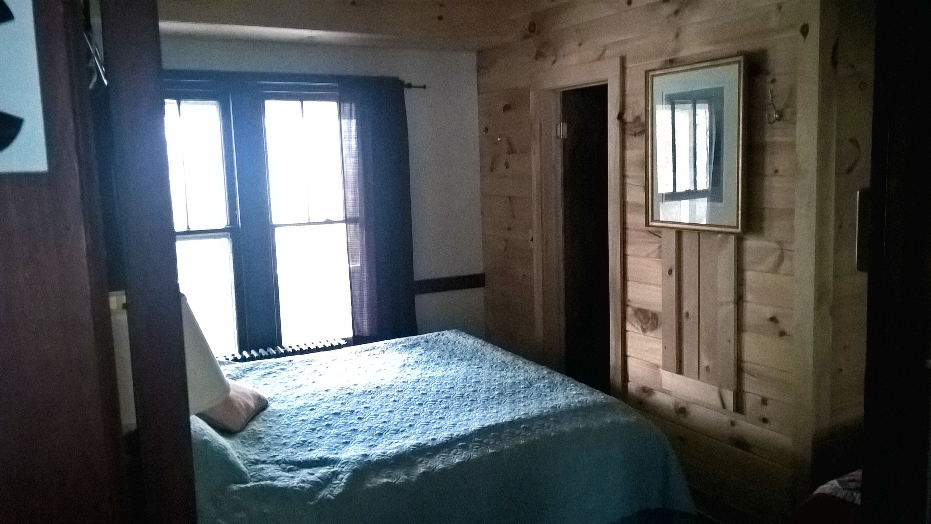 Una habitació amb un llit, parets de fusta, una finestra amb cortines i un mirall a la paret.