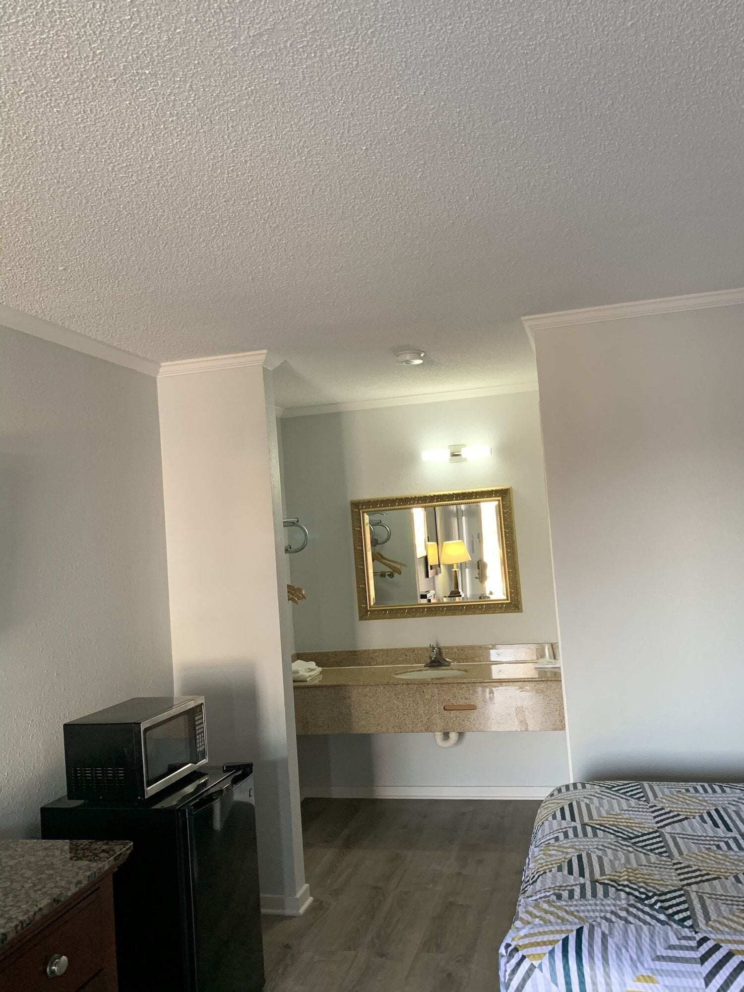 A hotel room with a bed, a desk with a microwave, a vanity with a mirror, and a sink.