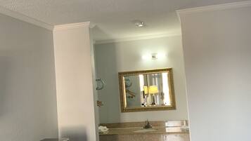 A hotel room with a bed, a desk with a microwave, a vanity with a mirror, and a sink.